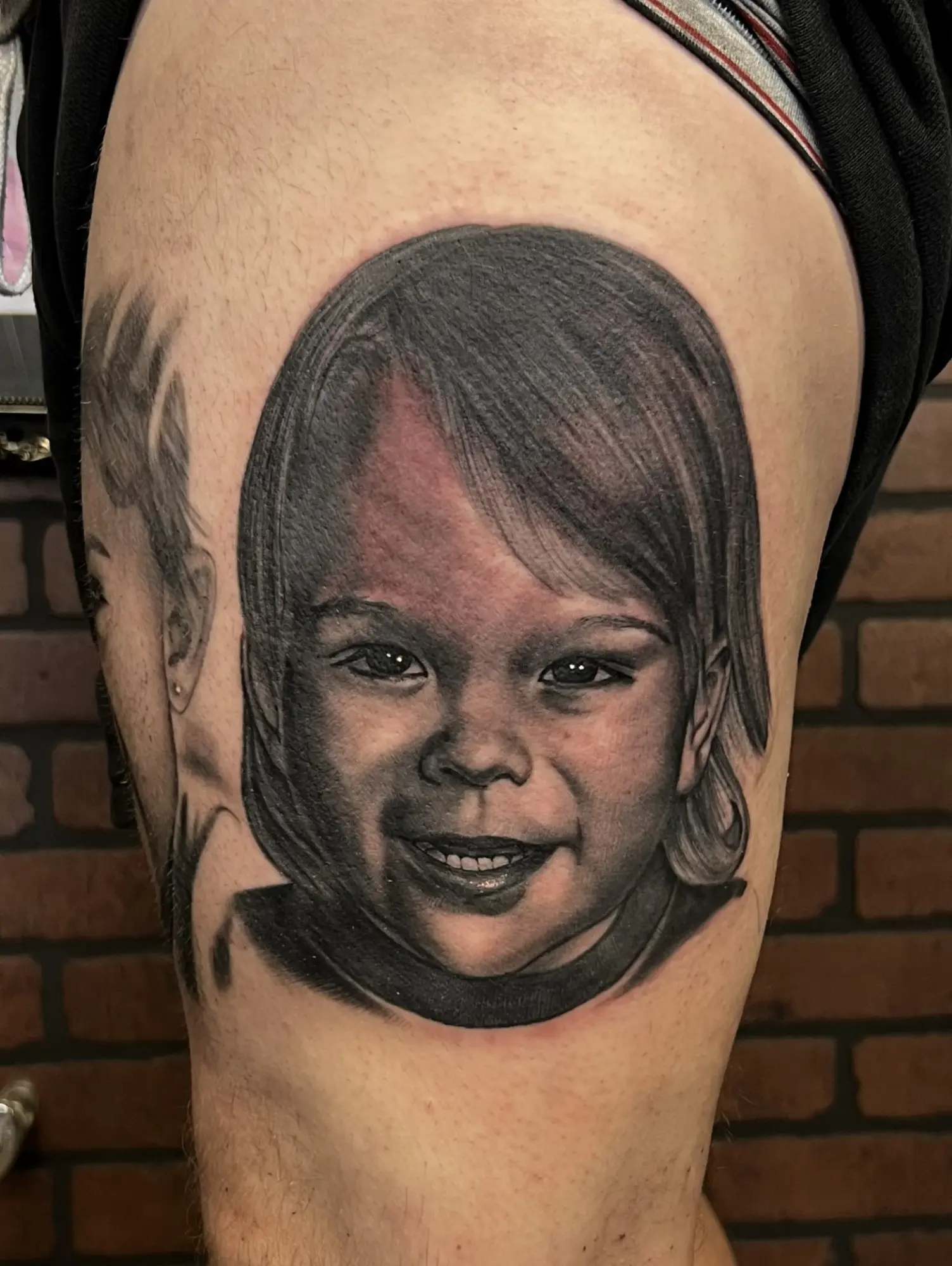 Black and grey portrait tattoo of a smiling child