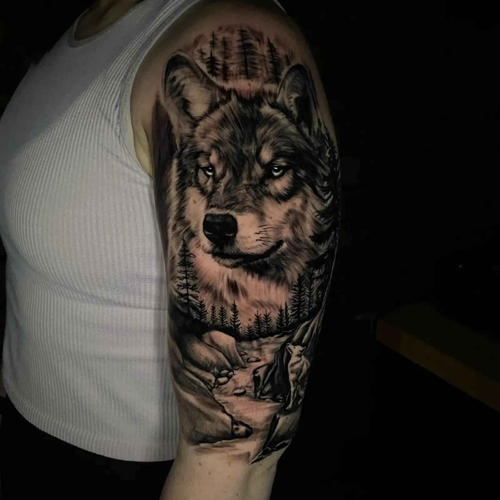 Black and grey wolf portrait upper-arm tattoo with a mountain landscape
