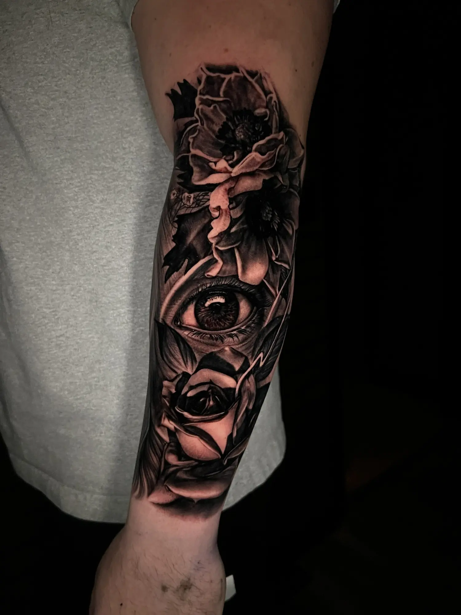 Black and grey illustrative forearm tattoo with roses, an eye, and a female portrait