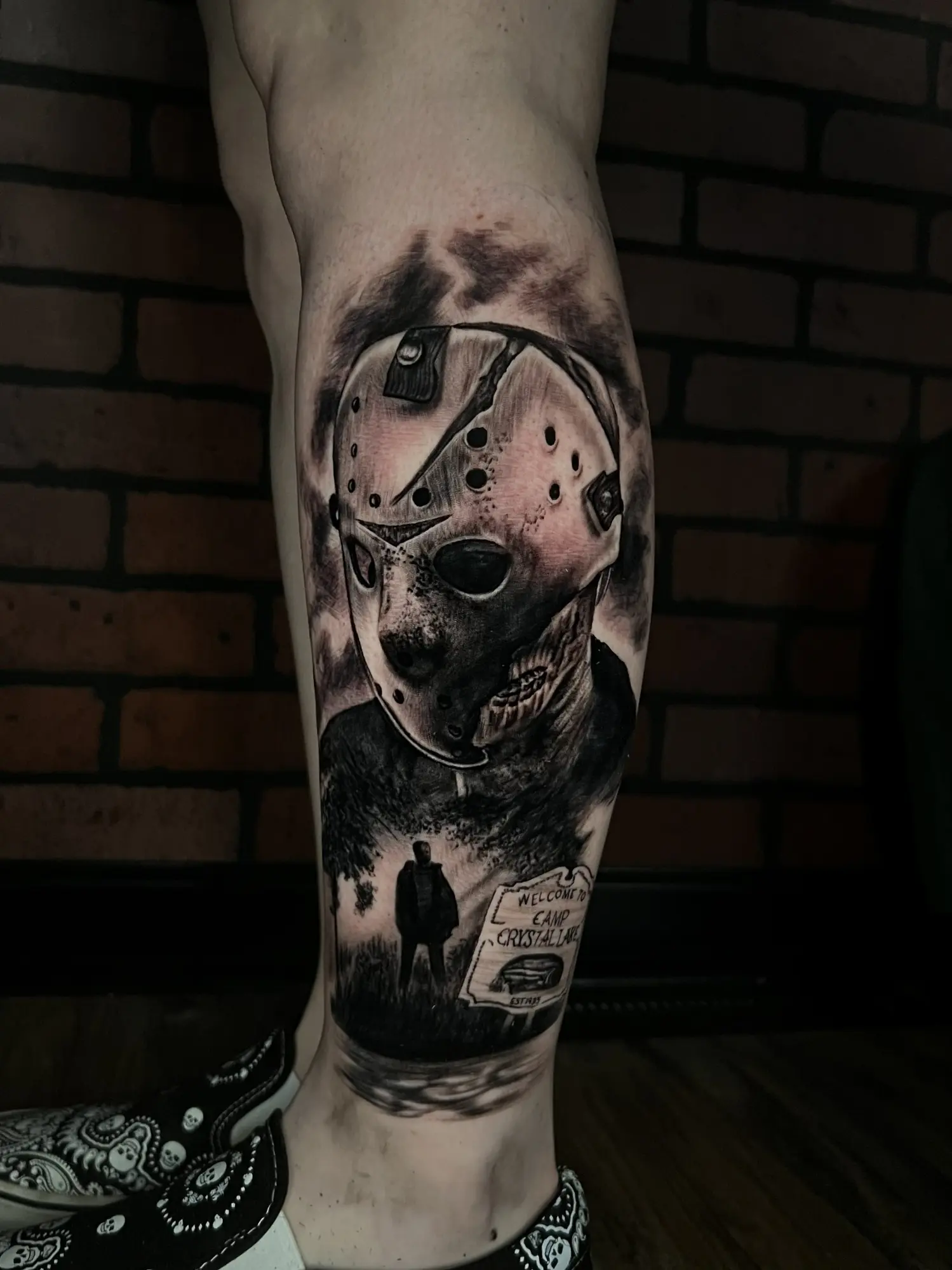 Black and grey horror tattoo with a hockey mask and cabin scene