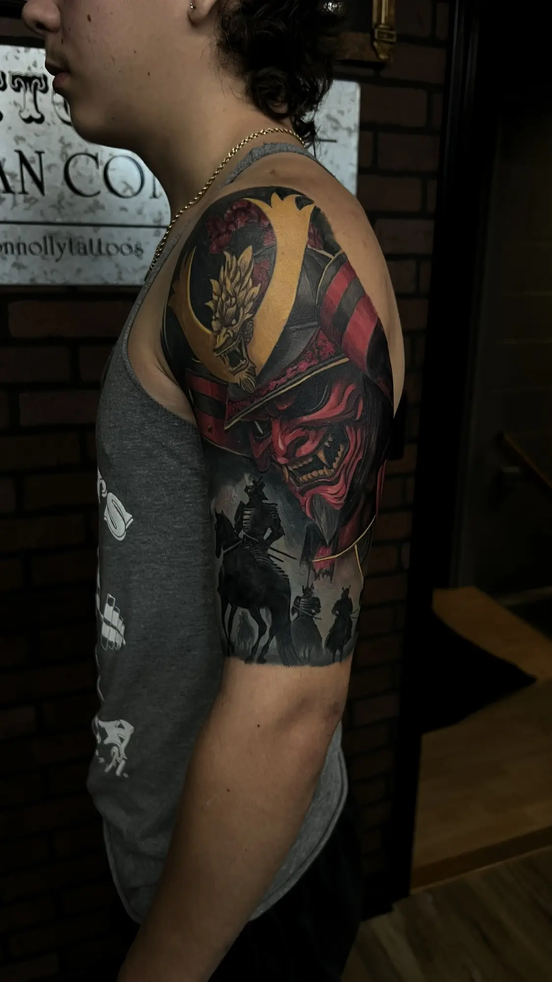 Color Japanese-inspired upper-arm tattoo with samurai and red oni imagery